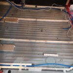 Boden ist entrostet, behandelt, mit Rostschutzfarbe gestrichen. Jetzt werden Kabel(-kanäle) verlegt und Holzteile auf den Boden geklebt, wo nachher die Bodenplatte und die Möbel darauf angeschraubt werden können.